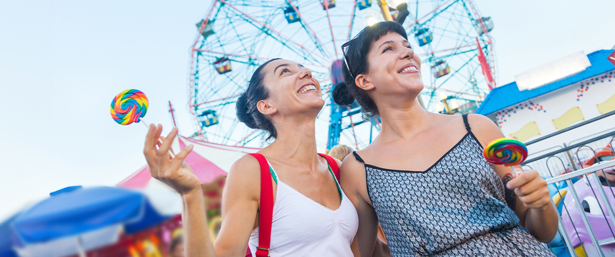 two women share a smile and enjoy lollipops at an amusement park